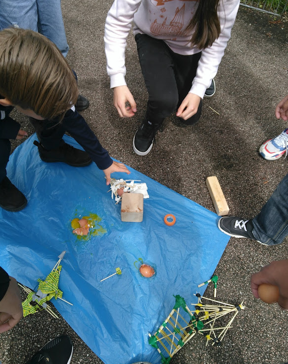 Students experimenting above a large blue plastic bag their egg-protectors from a falling brick.
